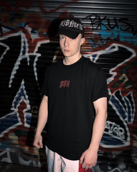A man in the black JPN Hannya Tee and a black cap standing in front of a graffiti-covered shutter