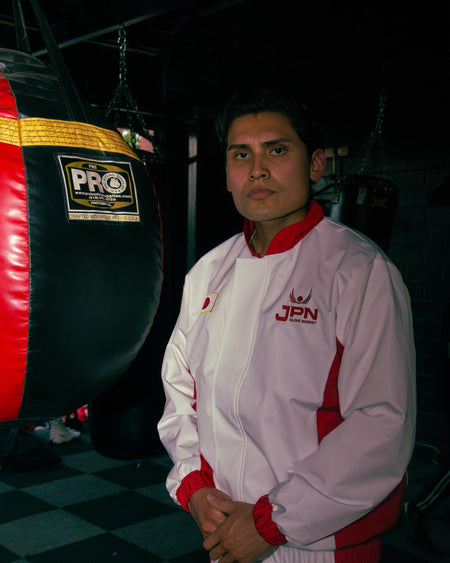 A fighter in the white and red JPN Team Japan track jacket beside a PRO heavy bag in a dark gym